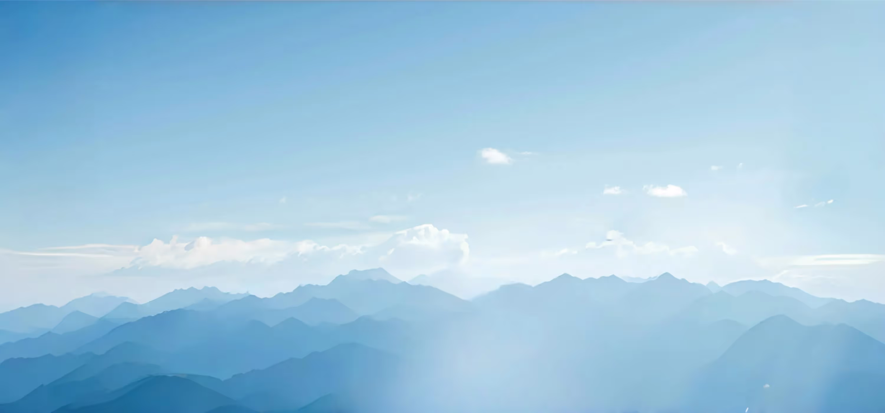 Blue-toned mountain range under a clear sky with scattered white clouds.