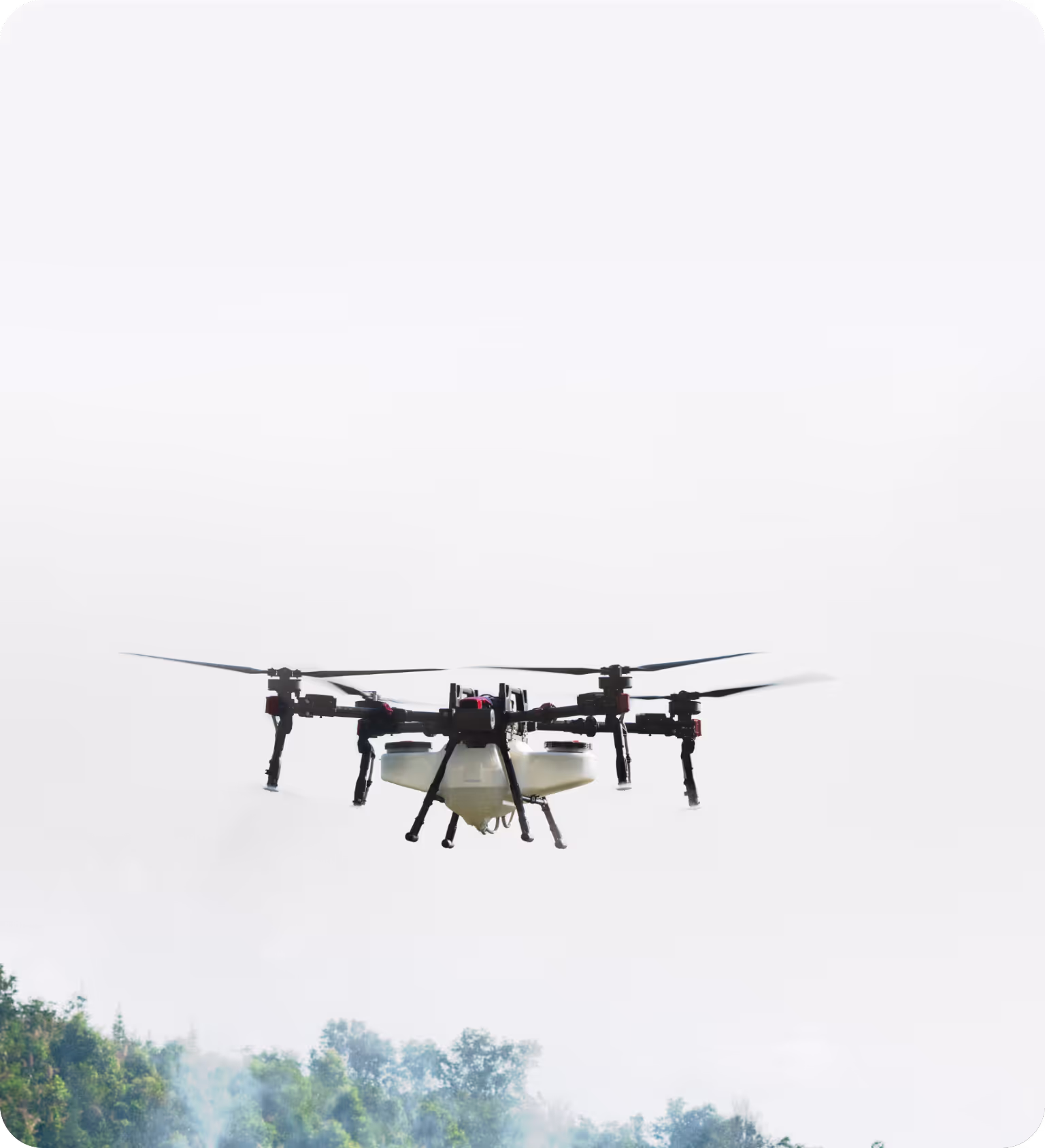 Drone with multiple rotors flying above a forested area against a white sky