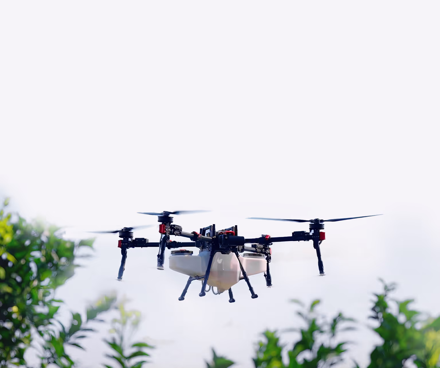 Quadcopter drone flying outdoors above green plants against a bright sky