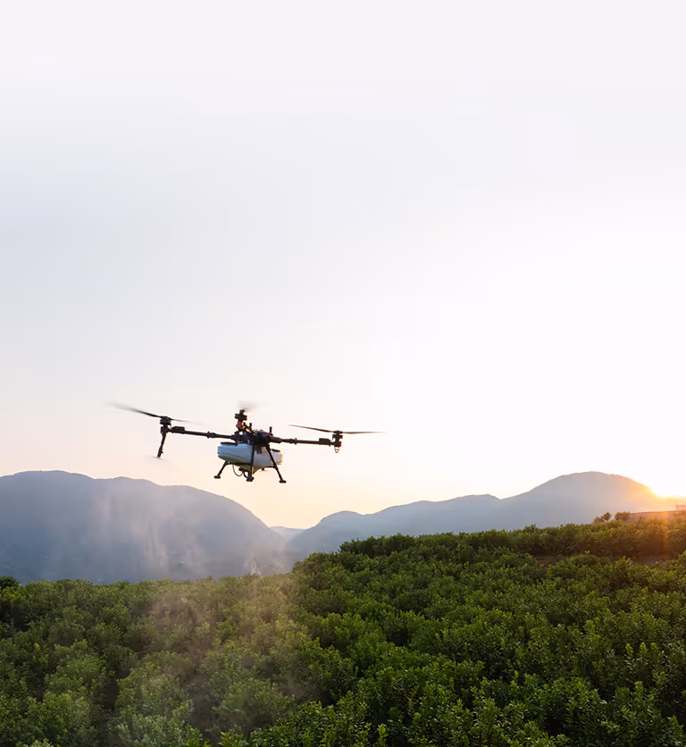 A drone with four rotors flying above trees under a clear sky.